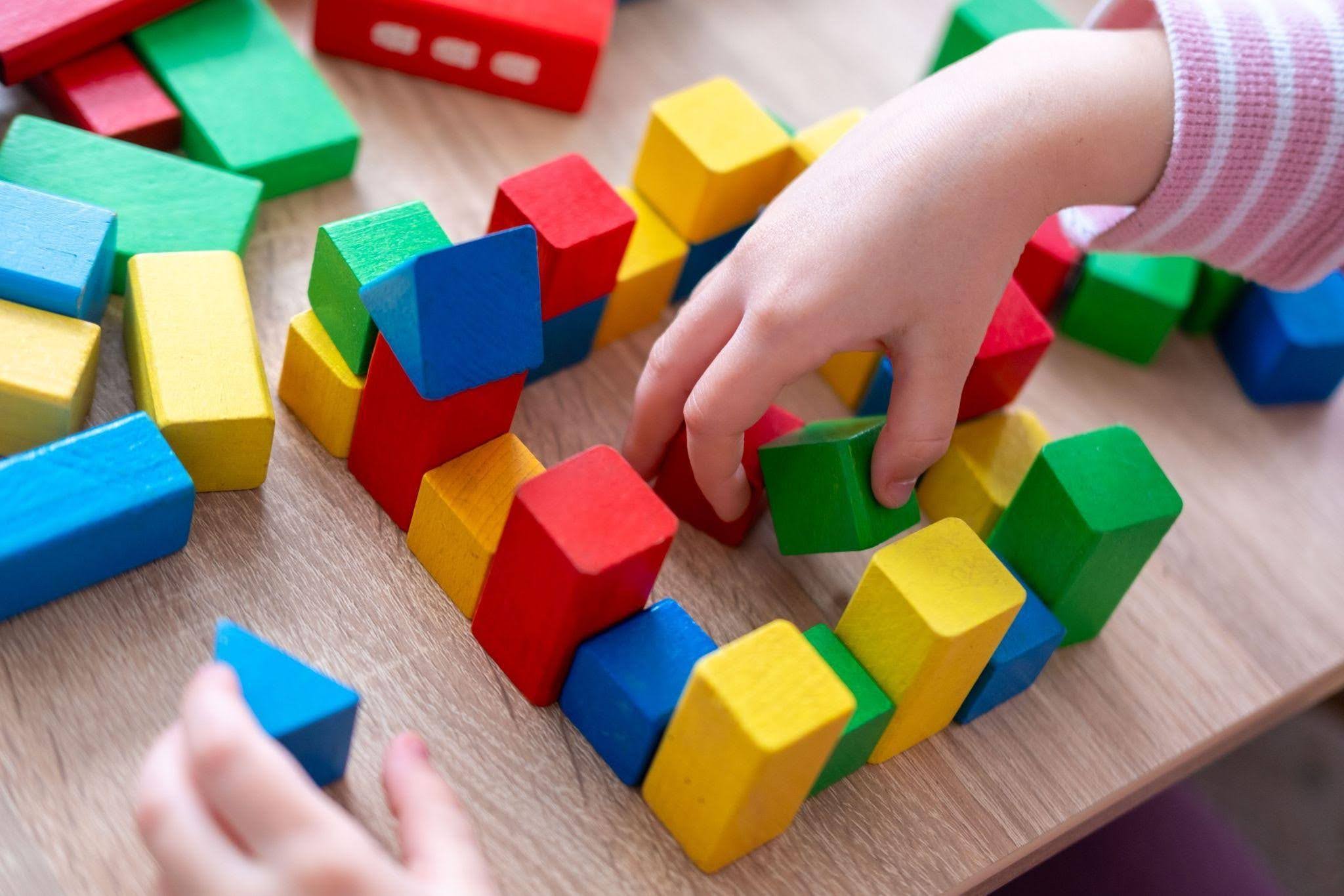 Child's hands playing with colorful wooden blocks scattered on a wooden table.